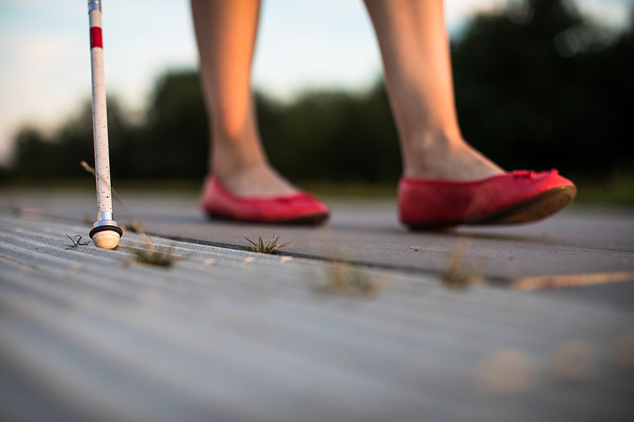 Blind woman walking on city streets, using her white cane to navigate the urban space better and to get to her destination safely